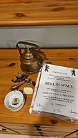 Photo showing vintage tin kettle, certificate for Berlin Wall fragment, metal bird figurines, and small decorative dishes