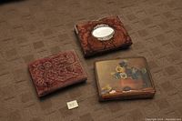 Three antique photo albums with various decorative covers displayed on carpet.