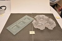 Top-down view of both glass dishes side-by-side. Rectangular dish on left, floral dish on right.