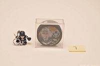 Front view of Curtis Joseph hockey puck in clear display case alongside Curtis Joseph goalie figurine keychain.