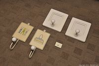 Four wall hooks arranged on carpet: two decorative laundry hooks with painted tiles and two white square photo hooks.