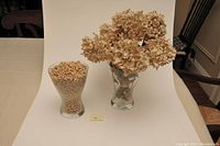 Two glass vases, one filled with dried beige hydrangea flowers, the other filled with cereal.