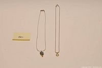 Two sterling silver necklaces laid flat side by side on a plain background with a yellow note showing '50'.
