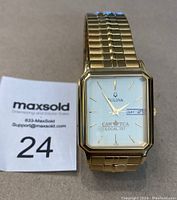 Gold tone rectangular Bulova wristwatch with day and date display, showing CAW TCA Local 707 logo on dial.