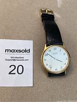 Full view of Seiko watch on a beige surface with black leather strap and gold-tone case, showing white dial with Arabic numerals and classic hands.