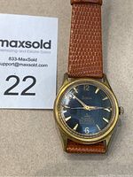 Front view of vintage Regina men's wristwatch with gold-tone case and brown leather band.