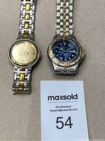 Photo of two men's wristwatches with two-tone stainless steel and gold metal bands, one with blue dial and the other with champagne dial.