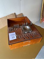 Top view of wooden base with various metal handcraft tools including ball-peen hammers, drill bits, a metal bowl tool, and a small gear piece, showing organization and usage wear.