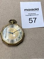 Front view of octagonal gold-tone pocket watch showing dial and hands