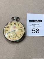 Front view of the vintage Marathon pocket watch showing the yellowed dial, black and red numerals, blue hands, and metallic case.