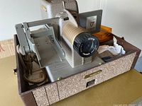 Two vintage 2x2 slide projectors inside a fitted carrying case, showing one projector front and side view.