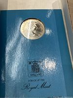 Silver coin featuring Queen Elizabeth II profile in blue Royal Mint holder with crest and text.