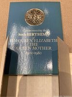 Photo showing the 1980 UK coin embedded in blue folder commemorating the Queen Mother's 80th birthday.