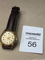 Photo showing the watch face and brown leather strap with a gold-tone case.