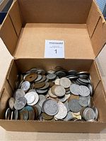 Box containing a large number of mixed world coins showing variety of shapes and sizes.