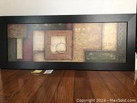 Full view of rectangular abstract print artwork in black wooden frame standing on floor.
