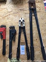Photo showing two pipe wrenches in red and black handles, and two bolt cutters side by side on a plywood surface.