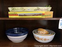 Shelf with vintage ceramic olive boat on top with grapevine design and four nested Pyrex mixing bowls with white and mustard floral pattern on lower shelf along with a blue and white large Pyrex salad bowl.