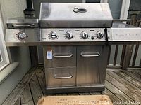 Front view of stainless steel Charbroil BBQ showing four burner control knobs and side burner knob, no lid handle visible, bungee cord attached on lid
