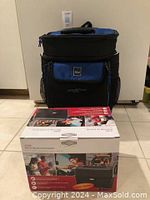Blue and black TLC Cool Carry portable cooler standing on a tiled floor with a 12 volt portable stove box in front.
