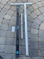 Drywall tools laid on a patterned stone surface showing a metal cutting square and two levels (black torpedo and white straight levels).