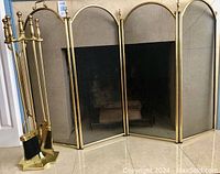 Full view of the four-panel solid brass fireplace folding screen in front of fireplace, with brass fireplace tools on stand next to it.