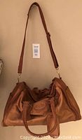 Full front view of brown leather bag with shoulder strap and top handles.