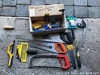 Overview of the lot with saws, box of cutters and scrapers, clamp, and hand tools