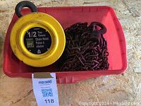 Photo of a half ton yellow chain hoist including attached chain and hooks inside a red plastic container.