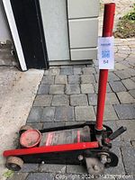 Master Craft floor service jack shown with handle lowered, placed on stone driveway, visible gauge and pumping mechanism.
