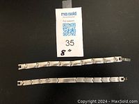 Two silver-tone metal bracelets laid out flat showing rectangular link design and clasp, 8 inch length indicated on tag.
