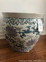 Side view of round ceramic planter showing floral and abstract design on cream base with flared rim and small feet.
