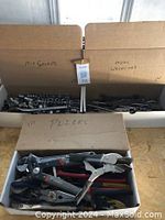 Three cardboard boxes labeled 'Misc Sockets,' 'Misc Wrenches,' and 'Pliers' with assorted hand tools inside