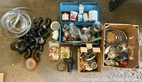 Overview of many miscellaneous plumbing parts including various black plastic pipe fittings, tubing, drain covers, tape, and small components in boxes and a blue plastic case.