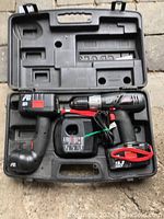 Open case showing cordless drill, cordless work light, and battery charger inside molded compartments.