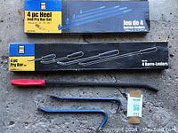 Photo of two boxed 4 pc pry and heel bar sets with bars laid out beneath on concrete