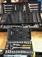 Front view of large and smaller Jobmate ratchet tool sets with sockets, wrenches, pliers, and bits displayed in black molded cases on a wooden surface