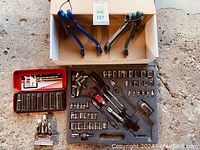 Two blue-handled ratchet tools above an open black molded case with ratchet and various sockets, extensions inside.