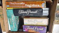 Photo showing multiple Trivial Pursuit editions stacked including DVD Pop Culture, Silver Anniversary, Genius IV and Genius V