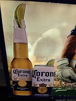 Close-up of Corona Extra beer bottle and can with lime wedge in illuminated sign.