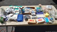 Wide view showing a table with various first aid supplies including blood pressure monitors, bandages, tapes, and pill organizers.
