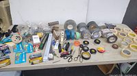 Overview of the assortment of tapes, glues, cutters, scissors and small hardware laid out on a table