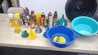 Photo of assorted automotive cleaning products including waxes, cleaners, sprays, cans, green and yellow funnels, blue oil pan and a light blue basin.