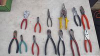 12 assorted pliers laid out on a flat surface, featuring multiple handle colors and types including needle nose and tin snips.