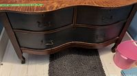Front view of antique wooden dresser showing curved front design with two small top drawers and two larger bottom drawers. Wood grain top surface with black drawer panels and metal handles.