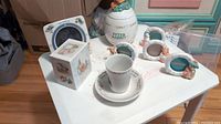 Photo showing all items arranged on a white table including Peter Rabbit jug, cup on saucer, photo frames, and box.