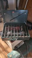 Coleman green metal portable stove with two burners and foldable wind guards, shown open and ready for use.