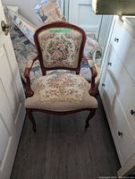 Front view of the vintage wooden chair with curved armrests and floral tapestry upholstery on the seat and backrest in a narrow room.