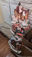 Multi-tiered Christmas village decoration with illuminated houses, showing snow details and winter scenery.