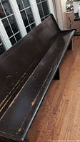 Wooden church pew showing whole length, dark finish, visible scratches and scuffs.